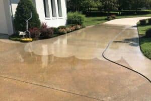 Power washing the driveway of a home in Chesapeake, VA. A surface cleaner attachment is actively removing dirt and grime, revealing a cleaner concrete surface.