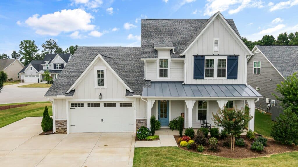 Two-story modern farmhouse with white siding, blue shutters, a gray roof, and a well-manicured lawn, illustrating the importance of house washing for maintaining curb appeal.
